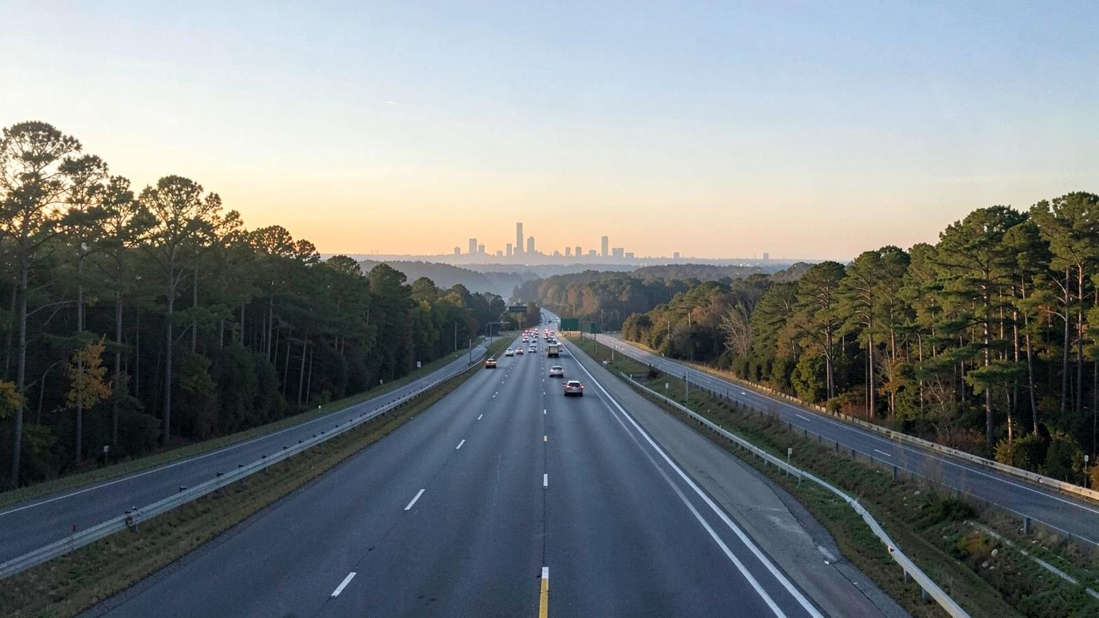 Multi-lane interstate highway through wooded Piedmont countryside with commuter traffic in morning light
