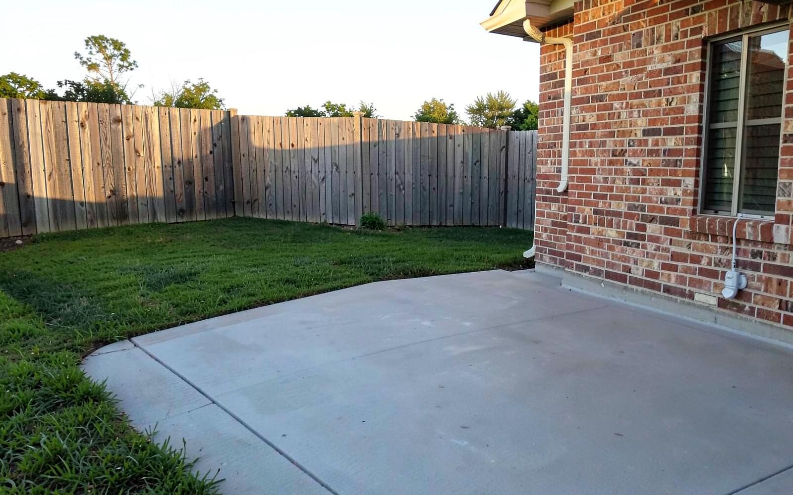 Backyard wooden privacy fence beside a freshly poured concrete patio at a brick Upstate home in late afternoon