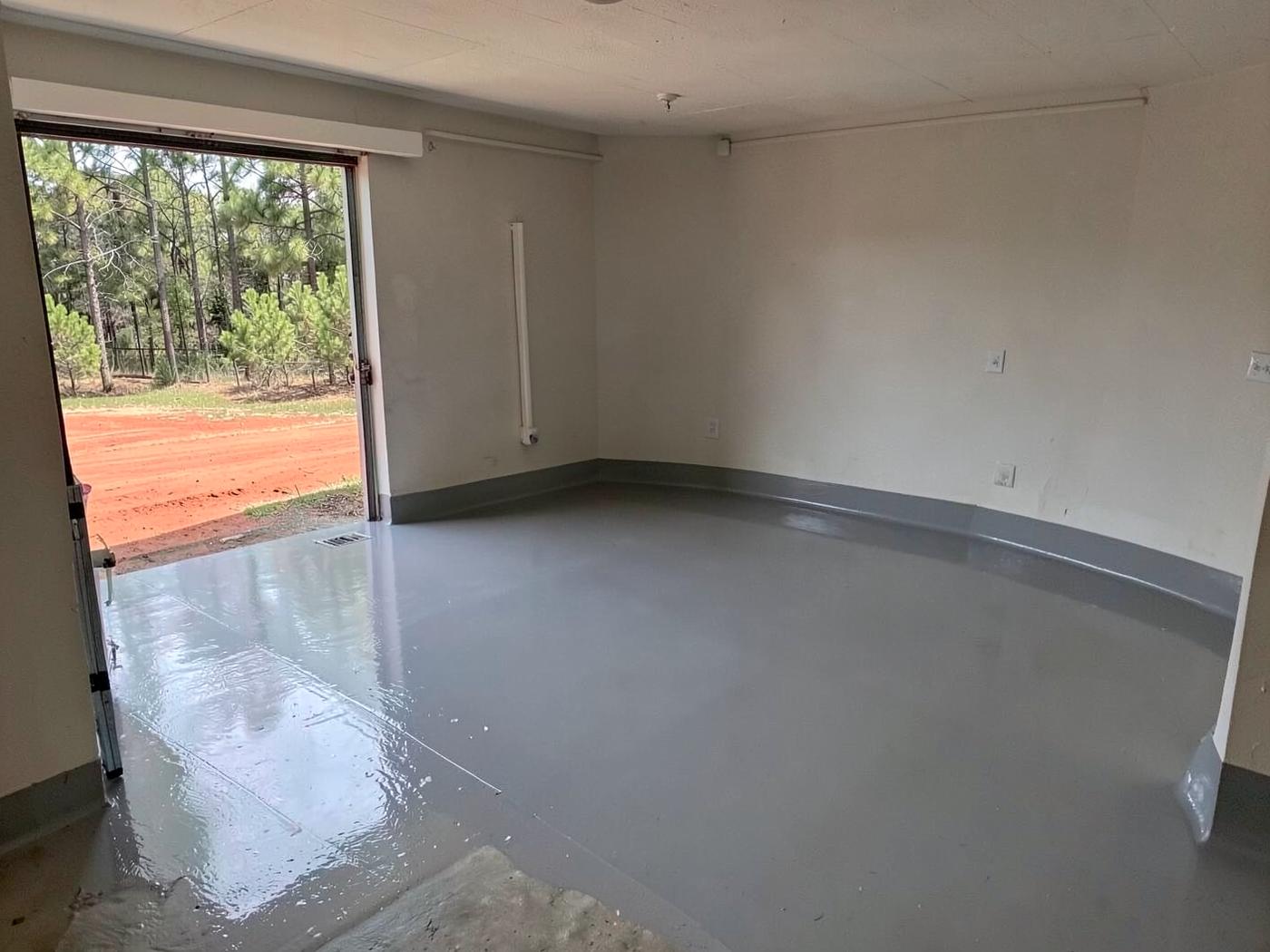 Glossy grey flake-coated garage floor inside an empty residential garage with the door raised to daylight