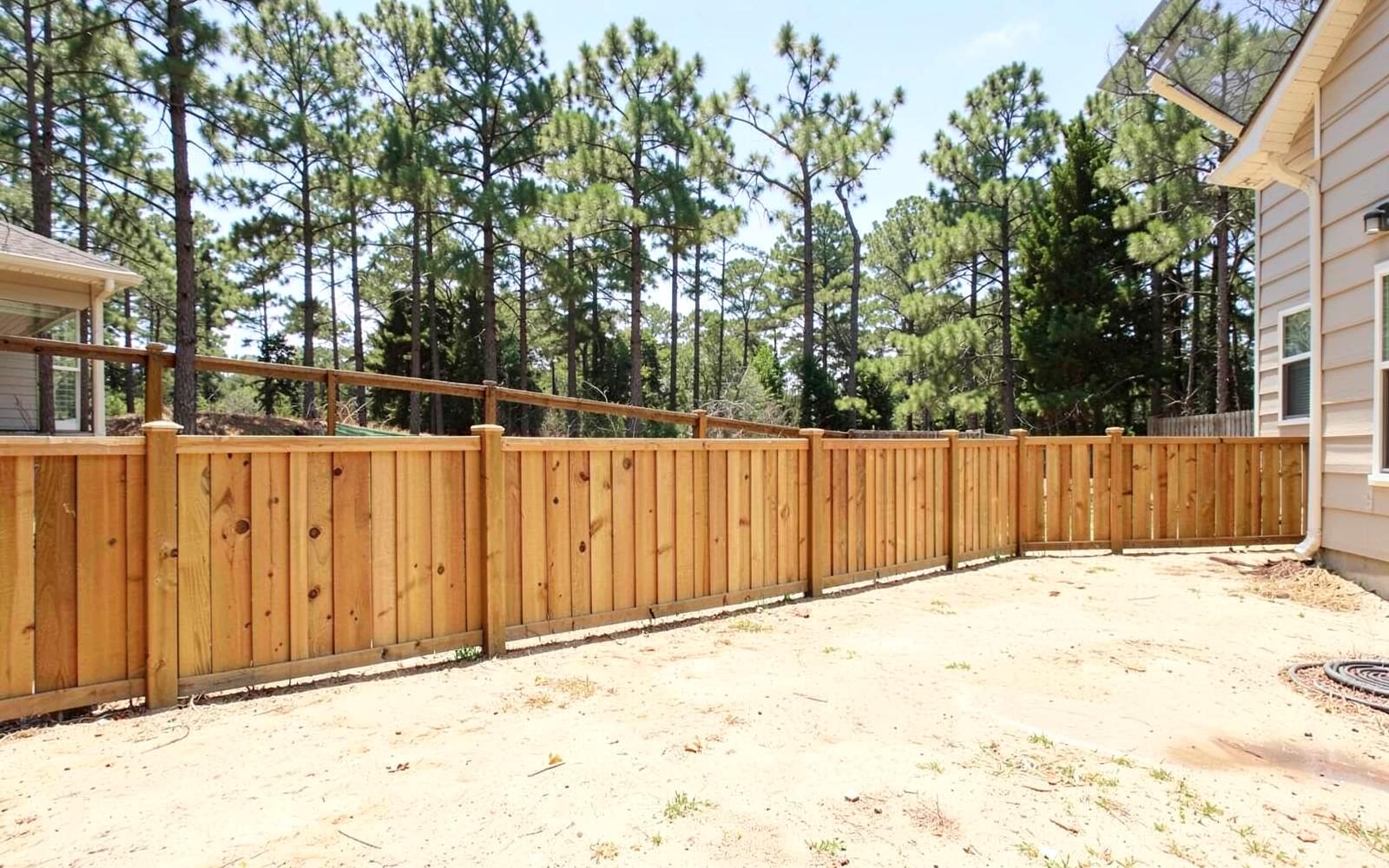 Freshly built wooden privacy fence running along the edge of a new yard on pale sandy soil