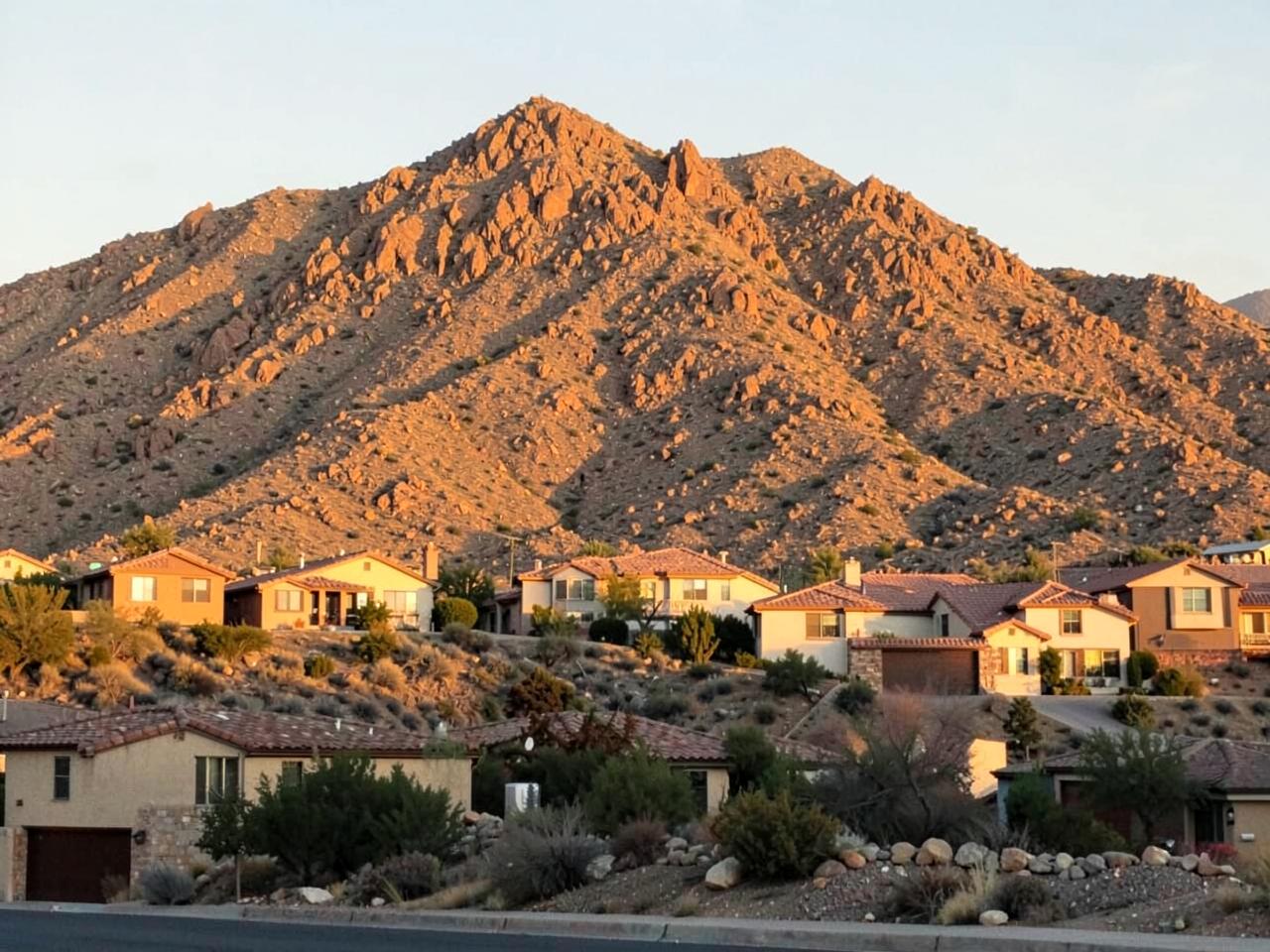 Rocky desert mountain rising behind a row of tile-roof suburban homes at golden hour