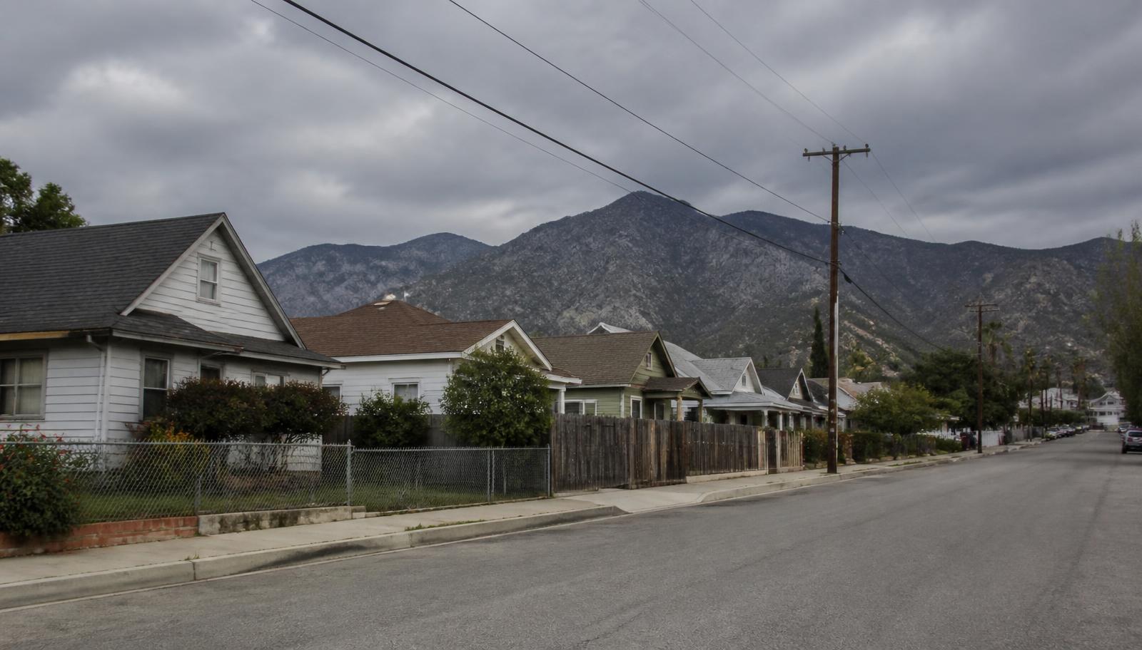 Long residential block of modest single-story homes with wood fencing and overhead power lines under a wide sky