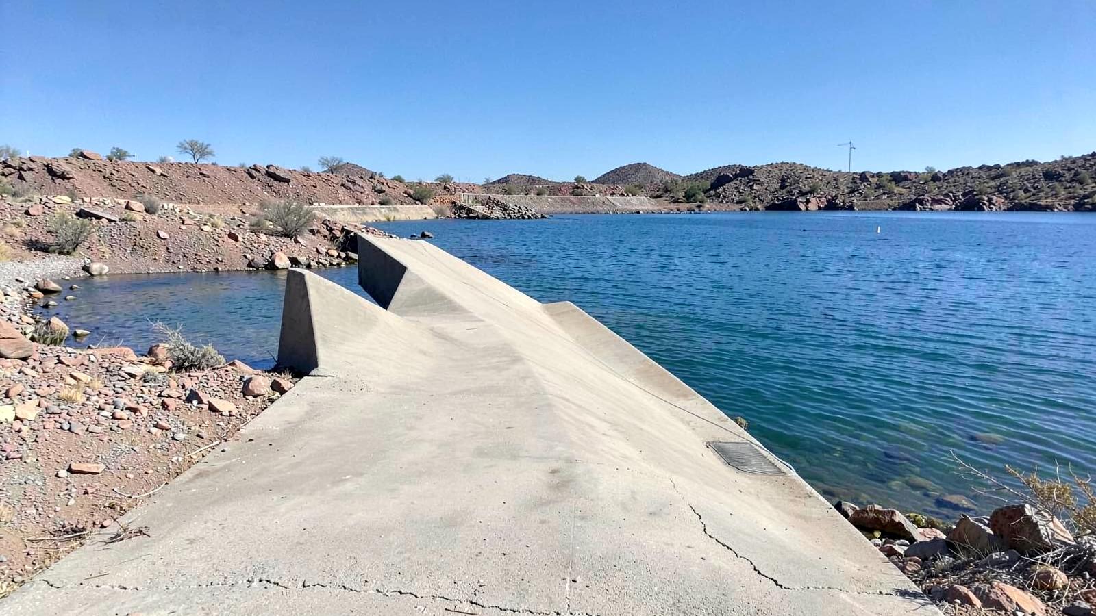 Empty concrete boat launch ramp sloping into bright blue desert lake water with a rocky shoreline