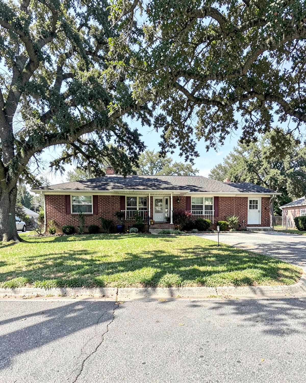 Mid-century red brick ranch house on a shaded Upstate South Carolina street with mature oak trees and a mown front lawn