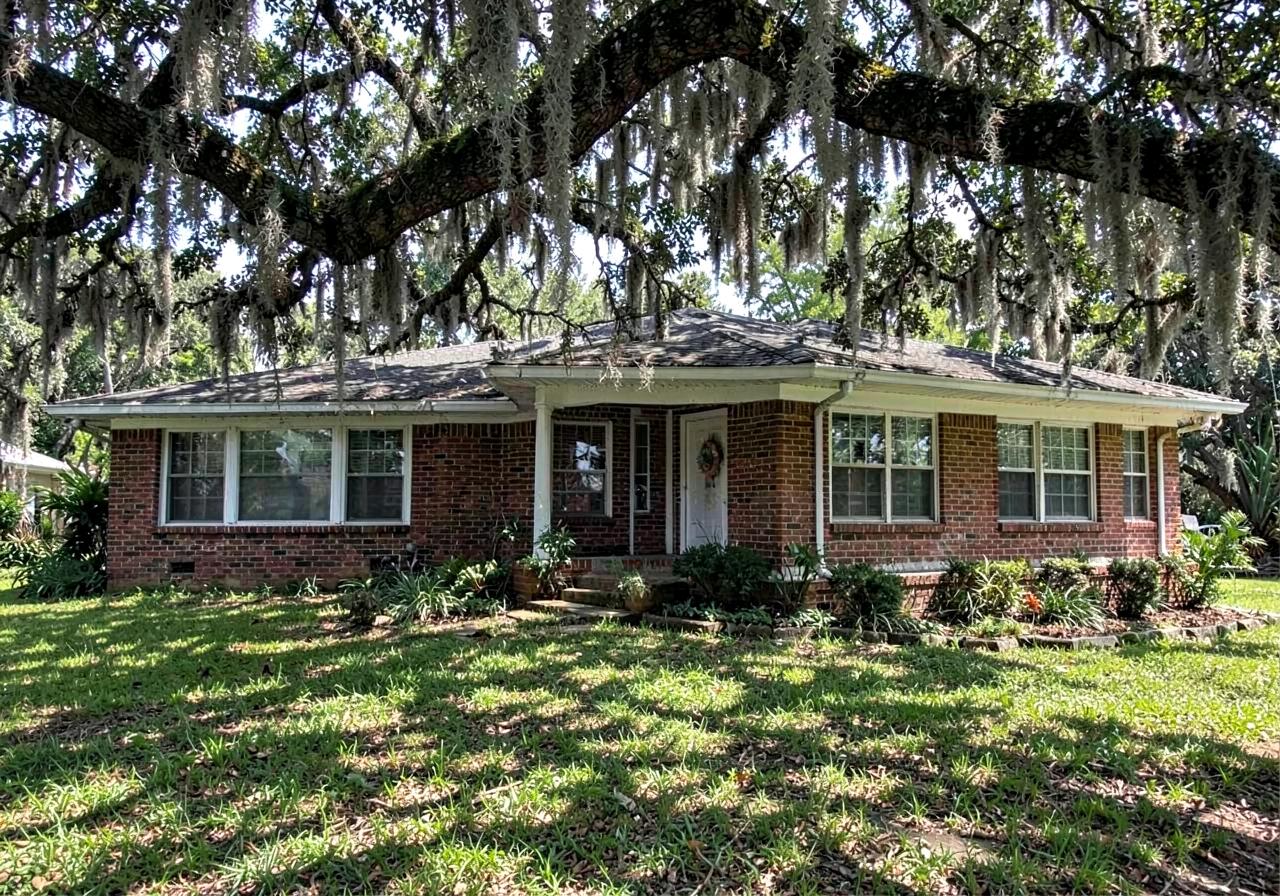 Brick single-story ranch house with white trim shaded by a large live oak draped in Spanish moss