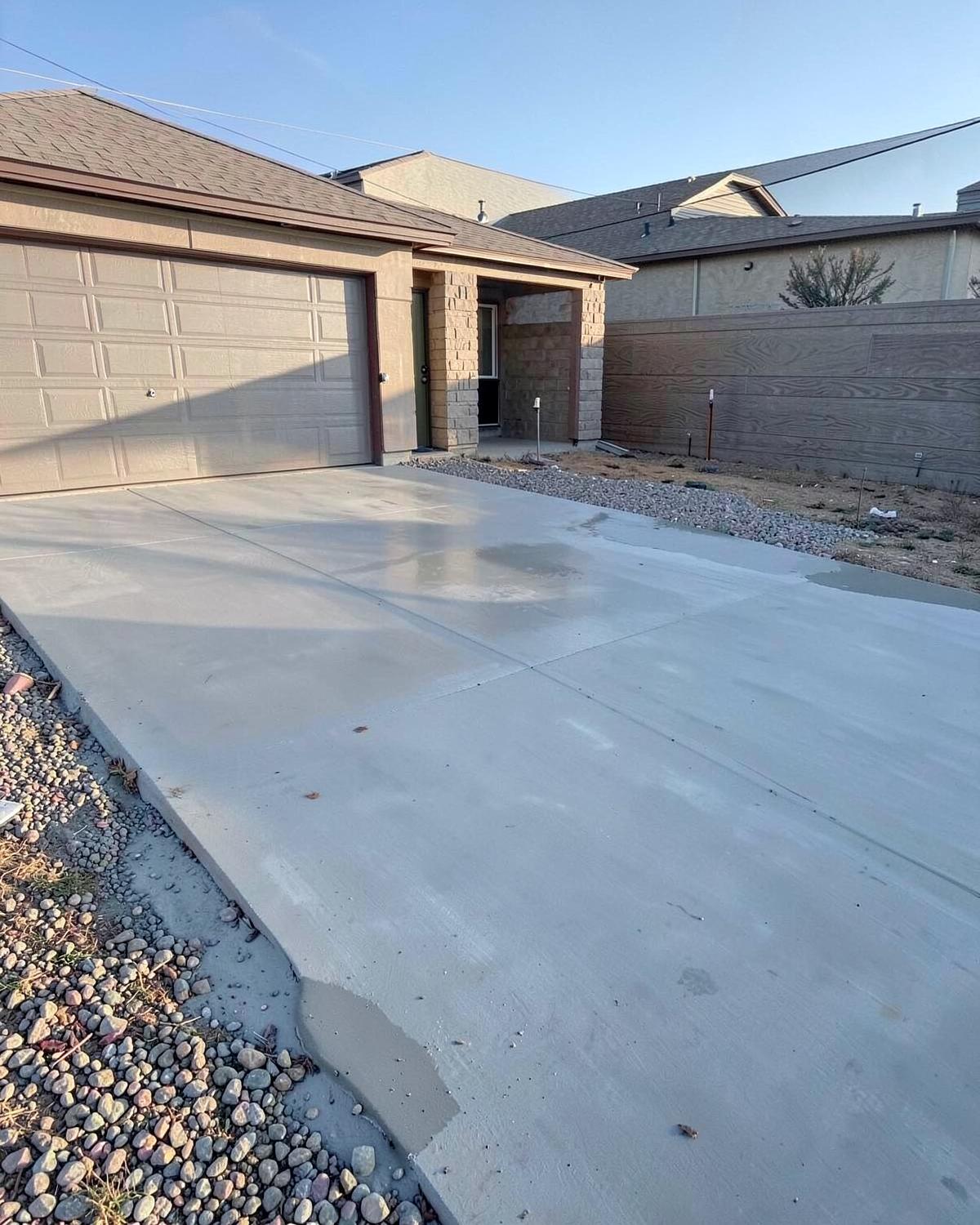 Freshly poured concrete driveway in front of a suburban garage on a dry gravel-edged lot