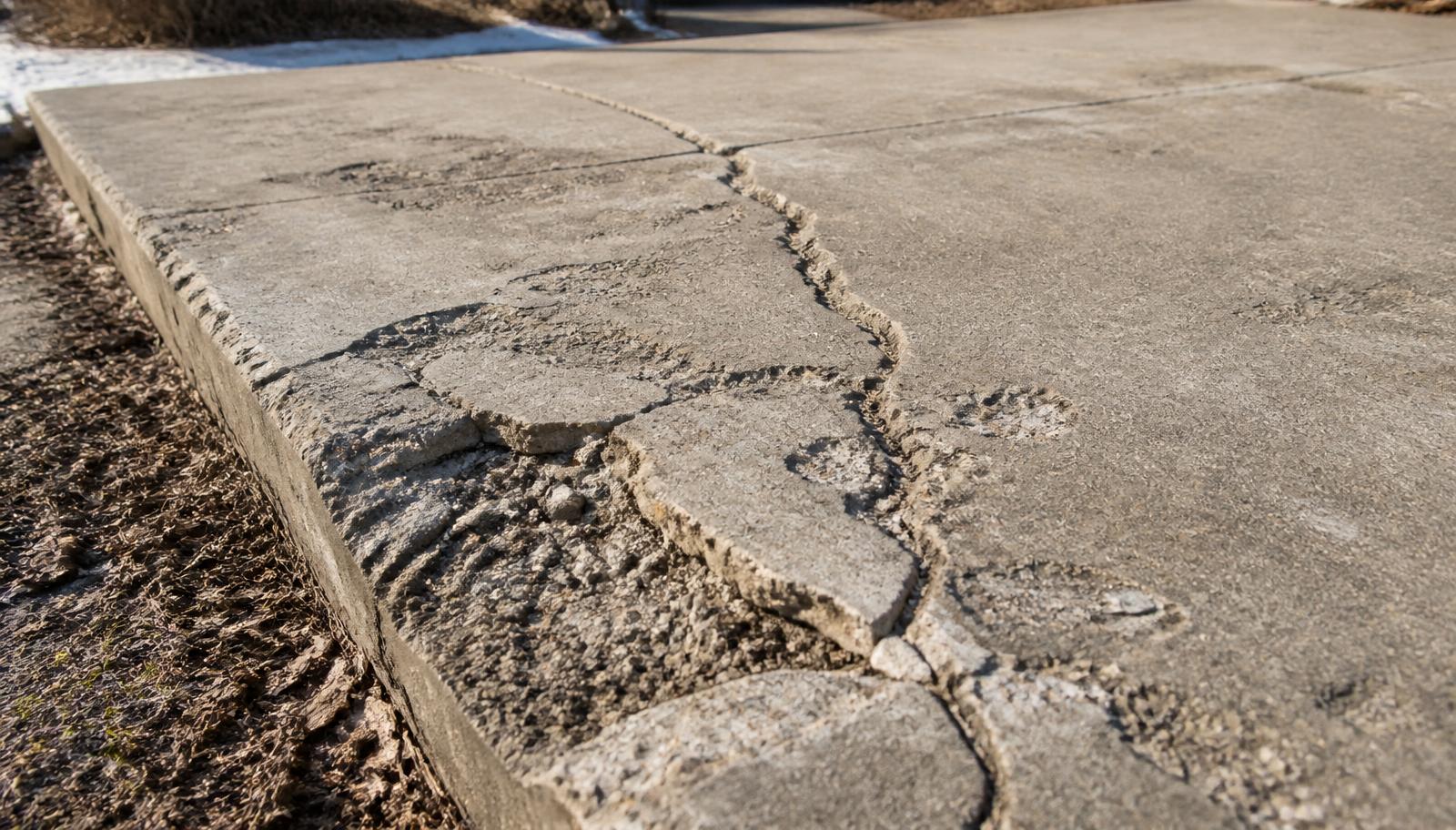 Freeze-thaw cracked concrete driveway apron outside a Salt Lake County home after a hard winter