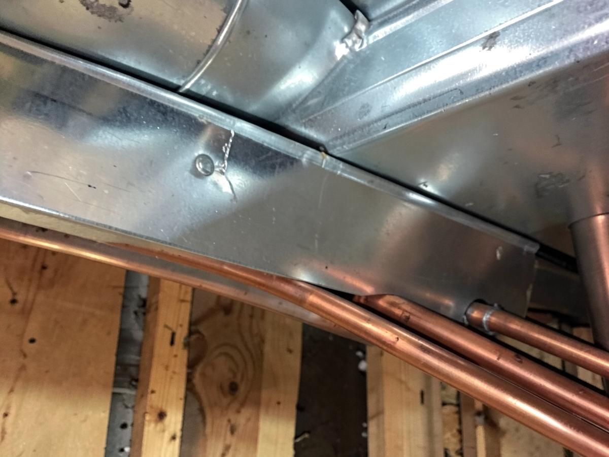 Galvanized heating ductwork and copper pipes running along wooden joists in a basement