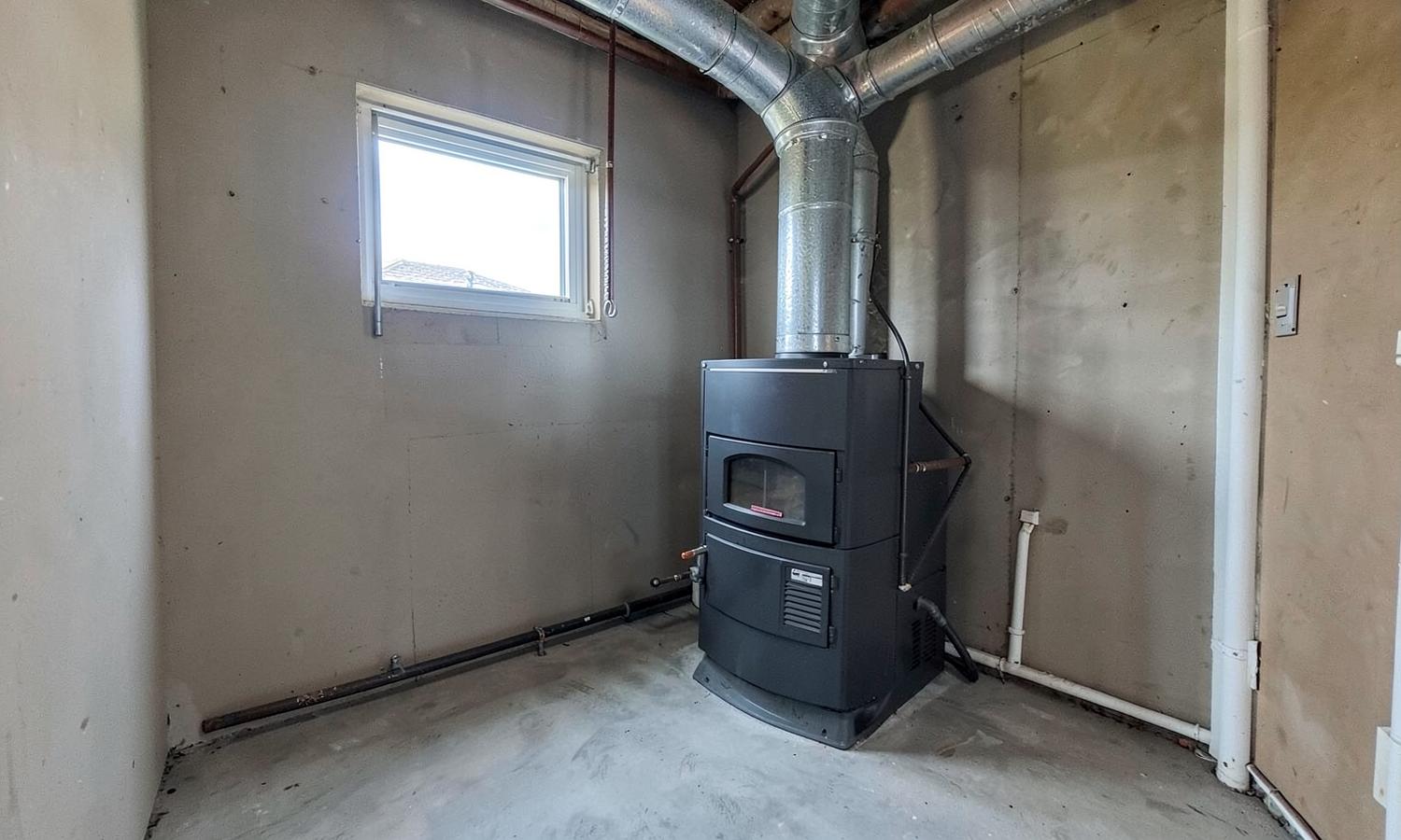 Gas furnace and sheet metal ductwork in the bare utility room of a modest home with insulated pipes and a concrete floor