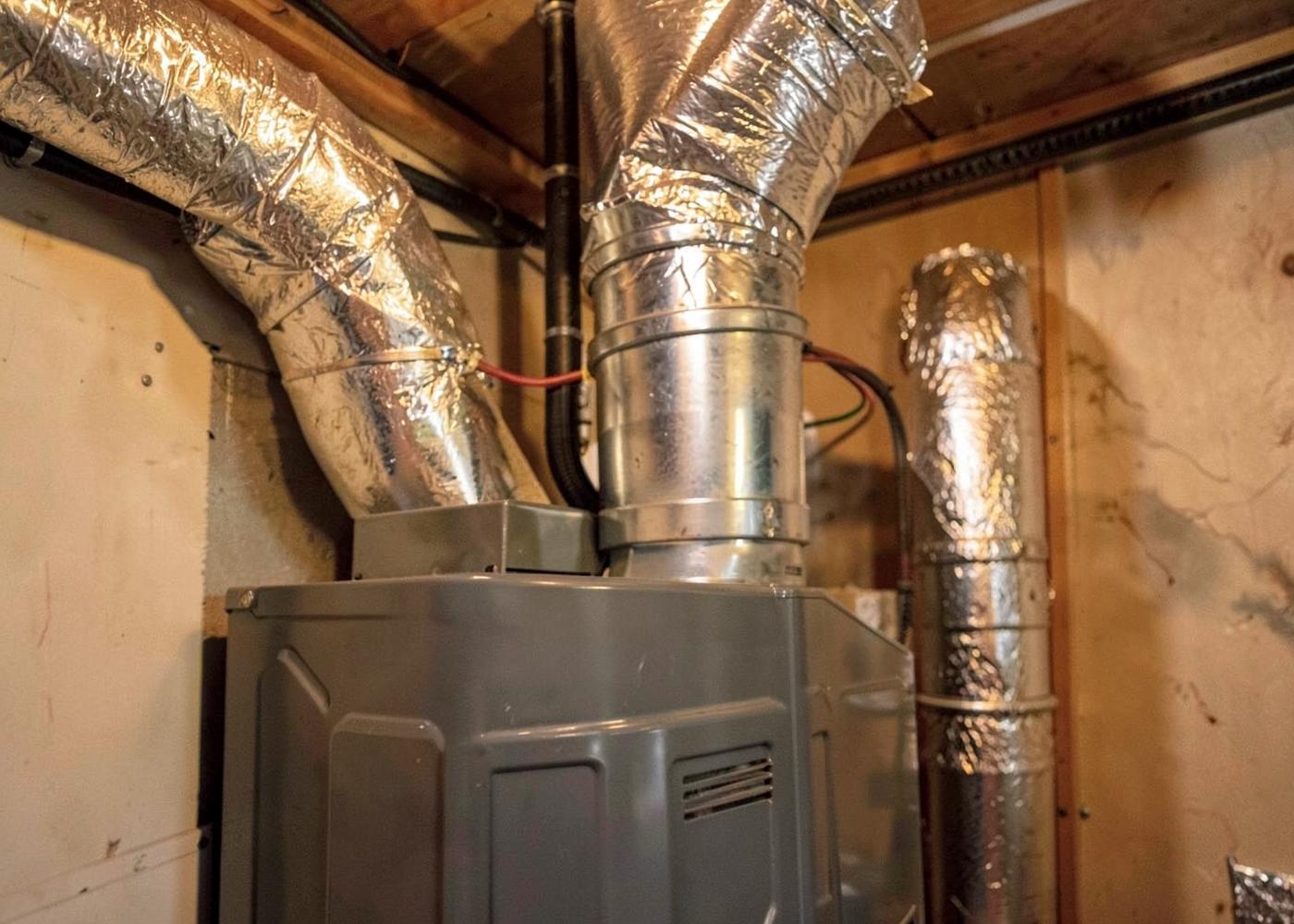 Close-up of a gas furnace and insulated ducting in a mountain home utility space lit by a work lamp