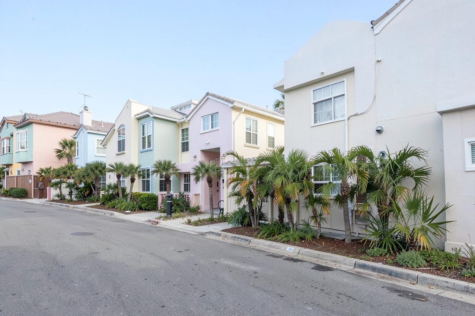 Quiet coastal street lined with pastel two-story vacation rental townhomes and palm shrubs