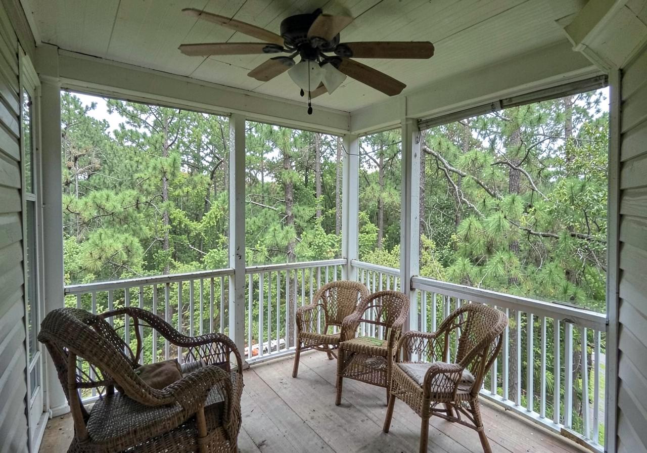 Screened back porch with a ceiling fan and wicker chairs looking out into dense green pines