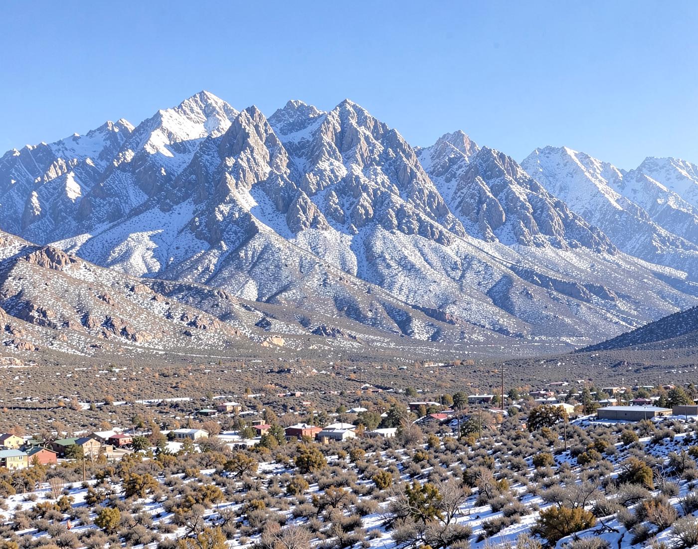 Wide desert valley floor with scattered rooftops below the long ridgeline of the Spring Mountains at golden hour