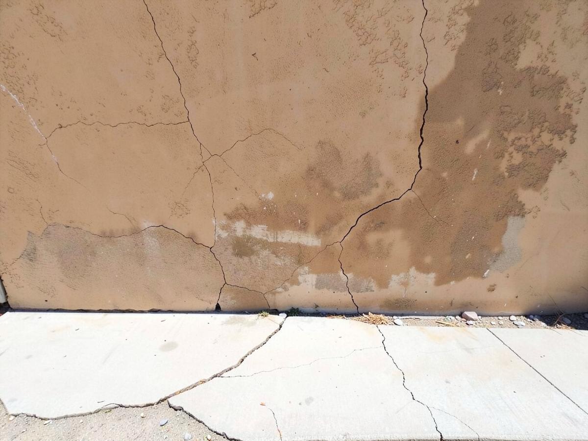 Sun-damaged tan stucco wall with hairline cracks above a cracked concrete walkway