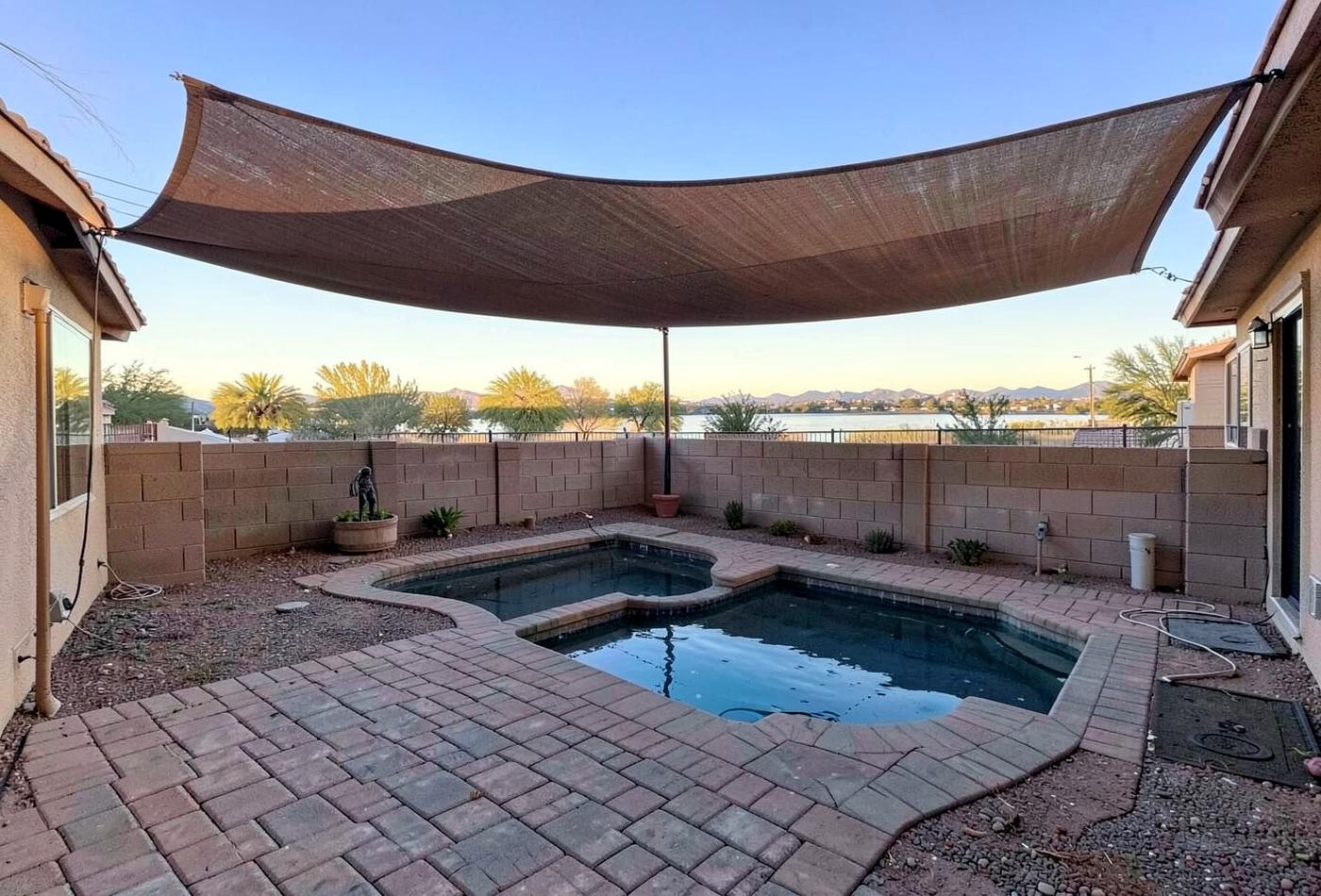 Desert vacation home backyard with a small pool, paver deck, shade sail and a lake view beyond a block wall
