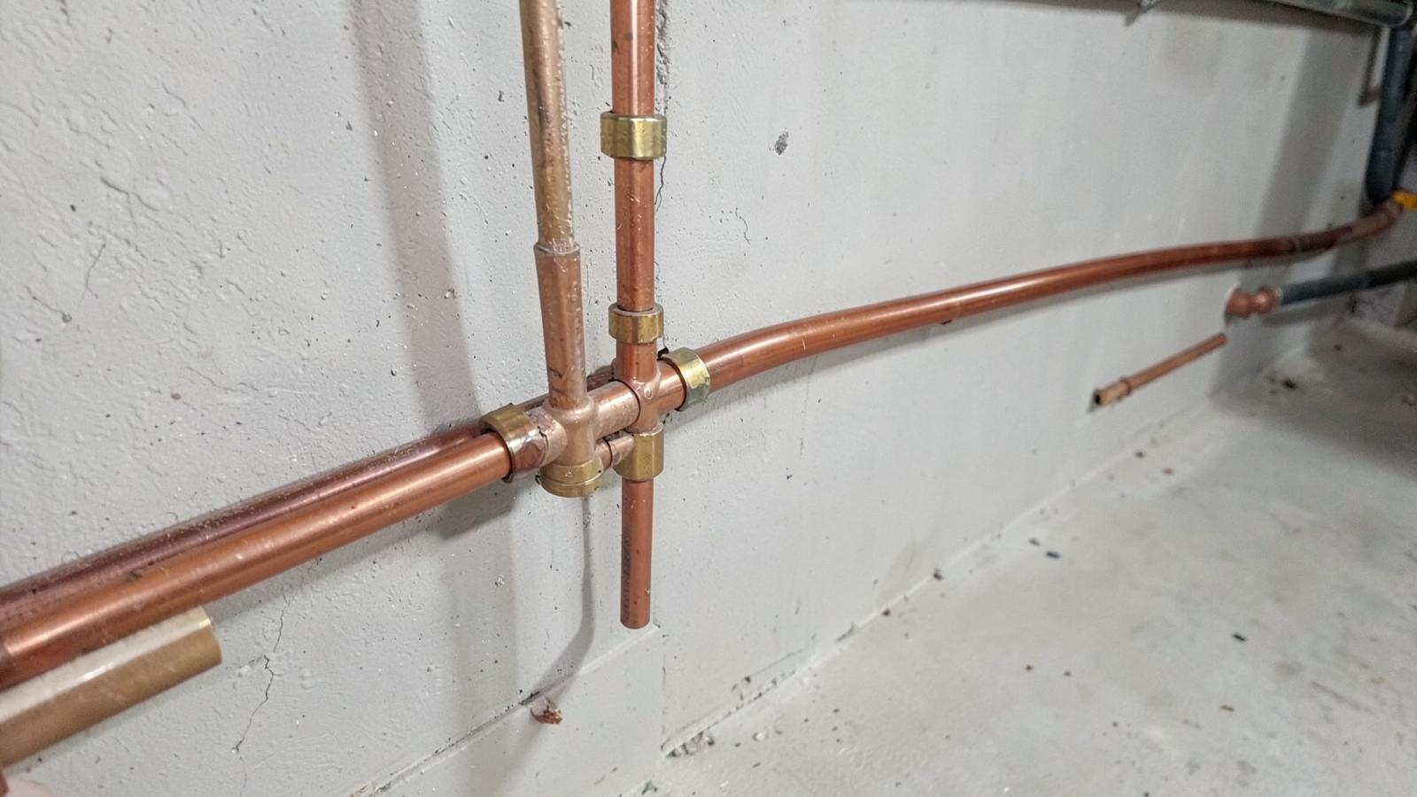 New copper water supply lines and brass fittings running along a clean basement wall