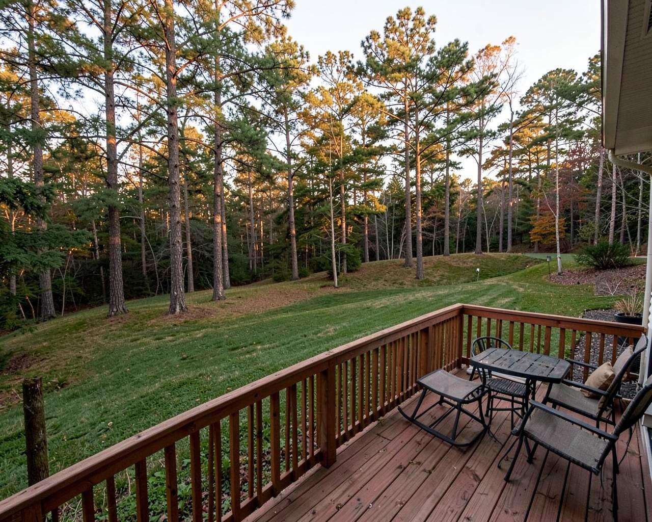 Wooden backyard deck with railing overlooking a sloped shaded lawn with tall pines at golden hour