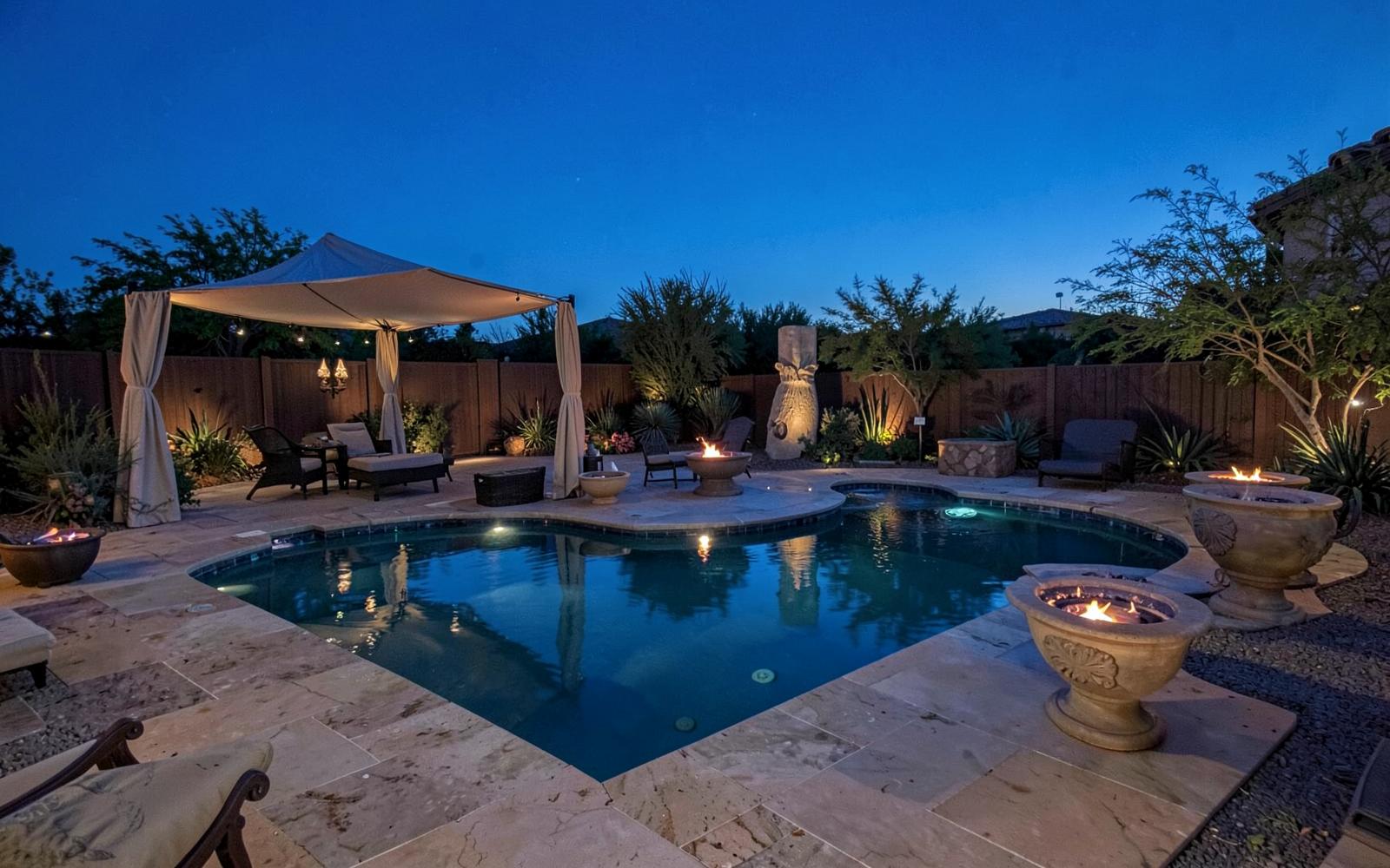 Luxury desert backyard pool with travertine deck, fire bowls and a shade cabana at blue hour