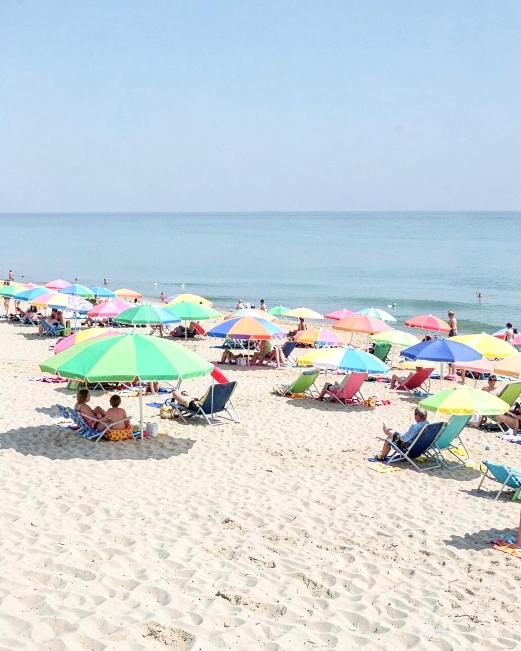 Rows of colorful beach umbrellas and chairs on wide pale sand beside calm Atlantic surf in summer