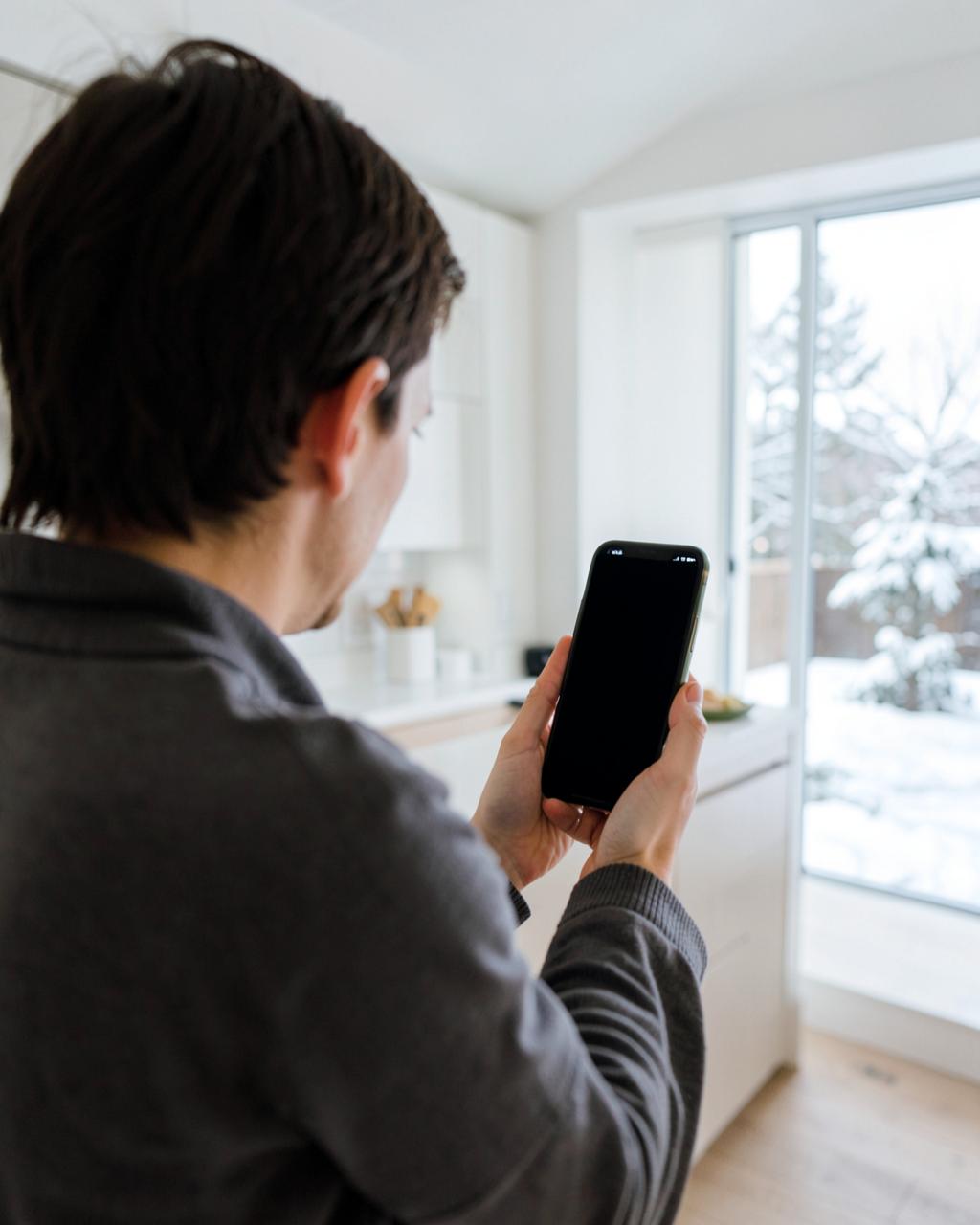 Hand holding a phone with a blank dark screen at a kitchen counter in soft morning light