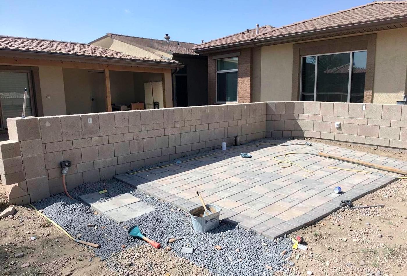 New block wall enclosing a gravel desert backyard with a paved patio and low desert plants in warm light