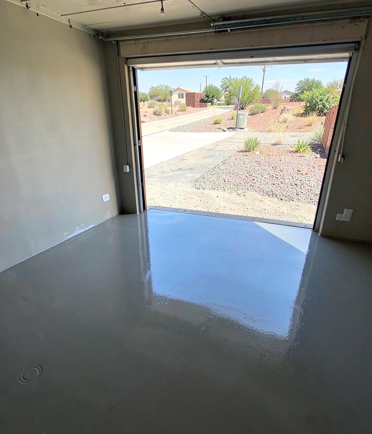 Freshly coated glossy grey epoxy garage floor with the door open to a bright desert driveway