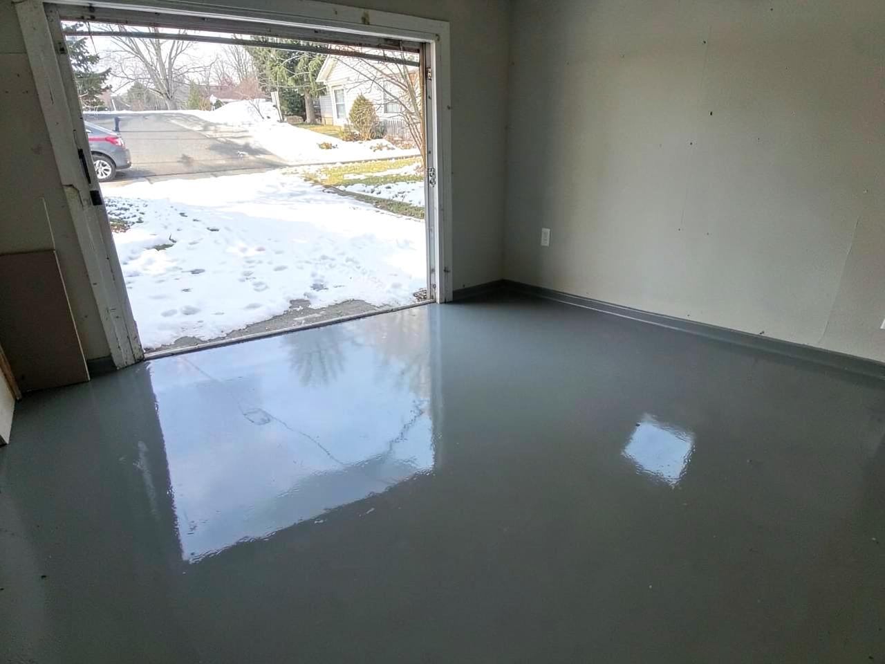Freshly coated glossy gray garage floor with the door open to a snow-covered driveway