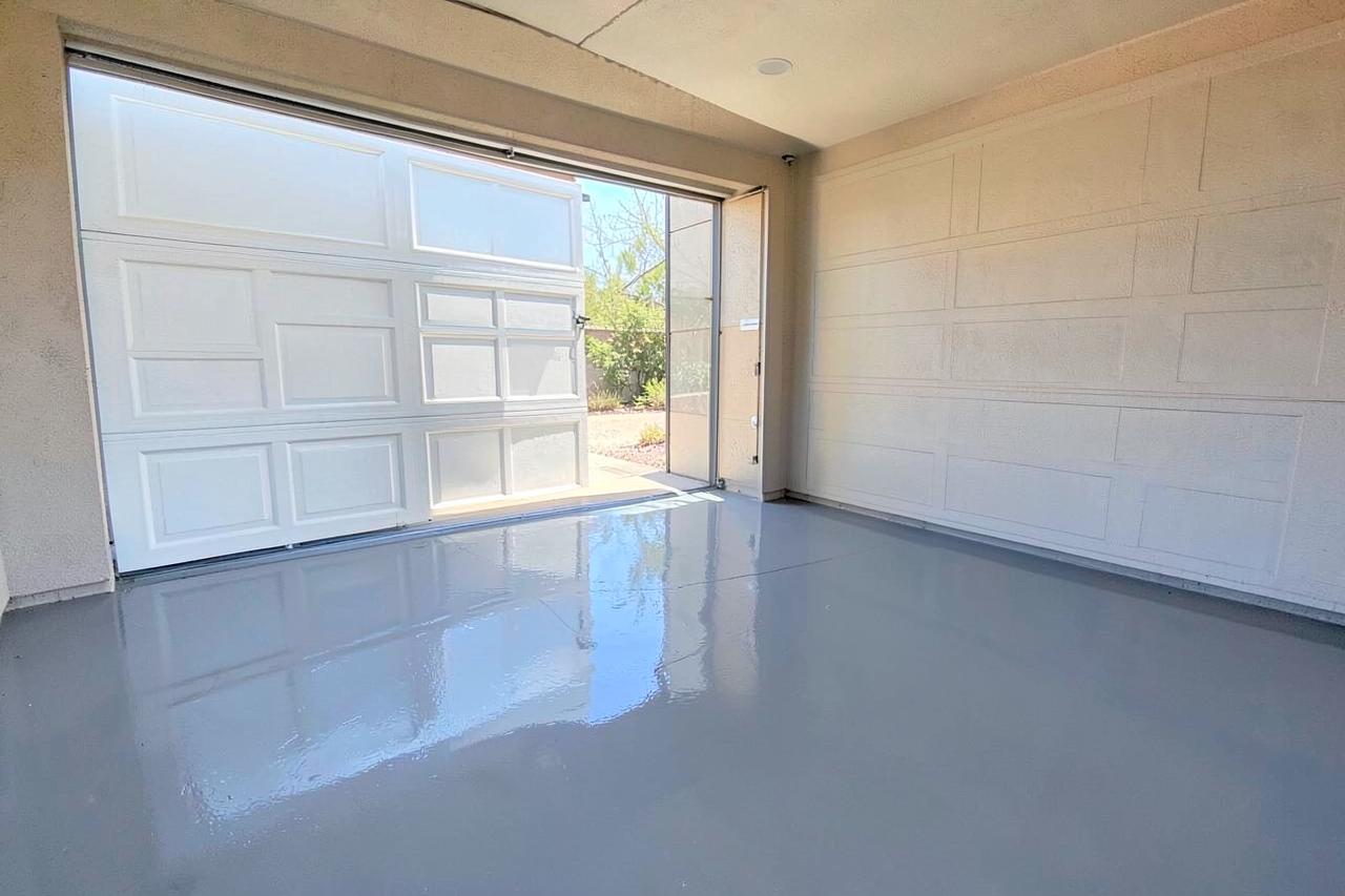 Glossy grey epoxy-coated garage floor in a clean suburban two-car garage with the door open to bright daylight