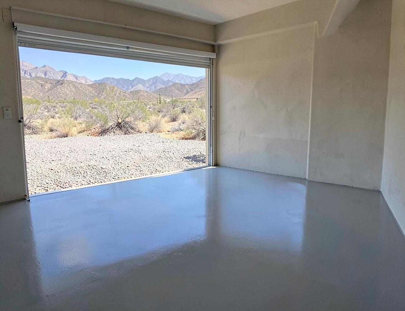 Glossy gray epoxy-coated garage floor in a clean desert garage with the roll-up door open to gravel and mountains