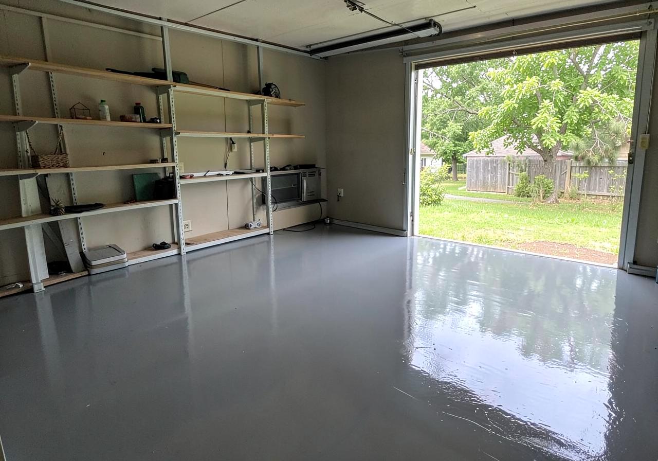 Glossy gray epoxy-coated garage floor with tidy shelving and daylight through the open door