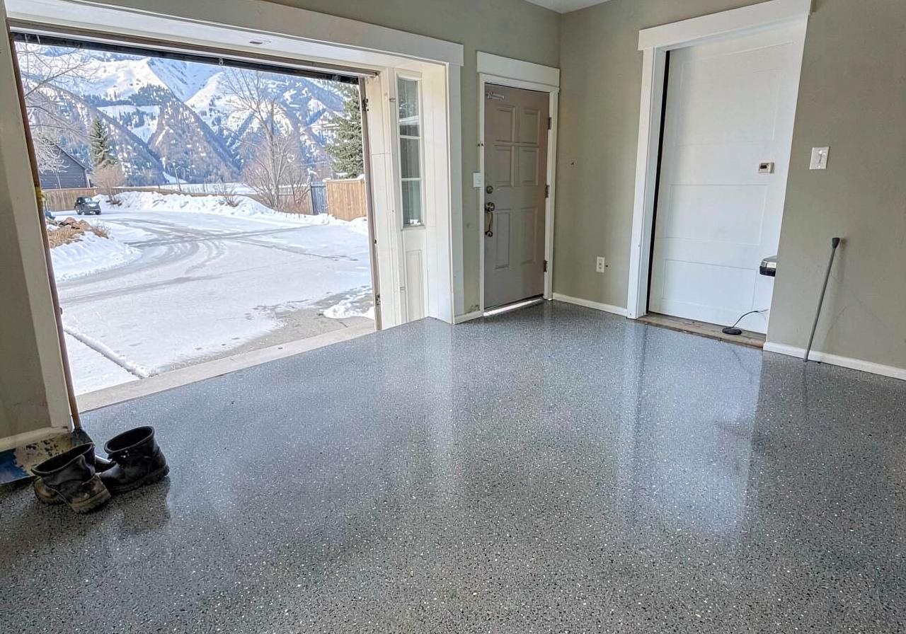 Glossy gray flake epoxy garage floor with the door open to a snowy driveway and mountains beyond
