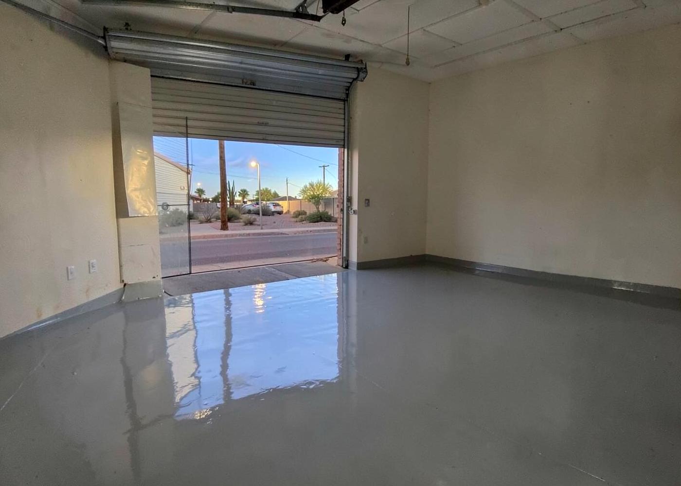 Glossy gray epoxy-coated garage floor in an empty two-car garage with the roll-up door open