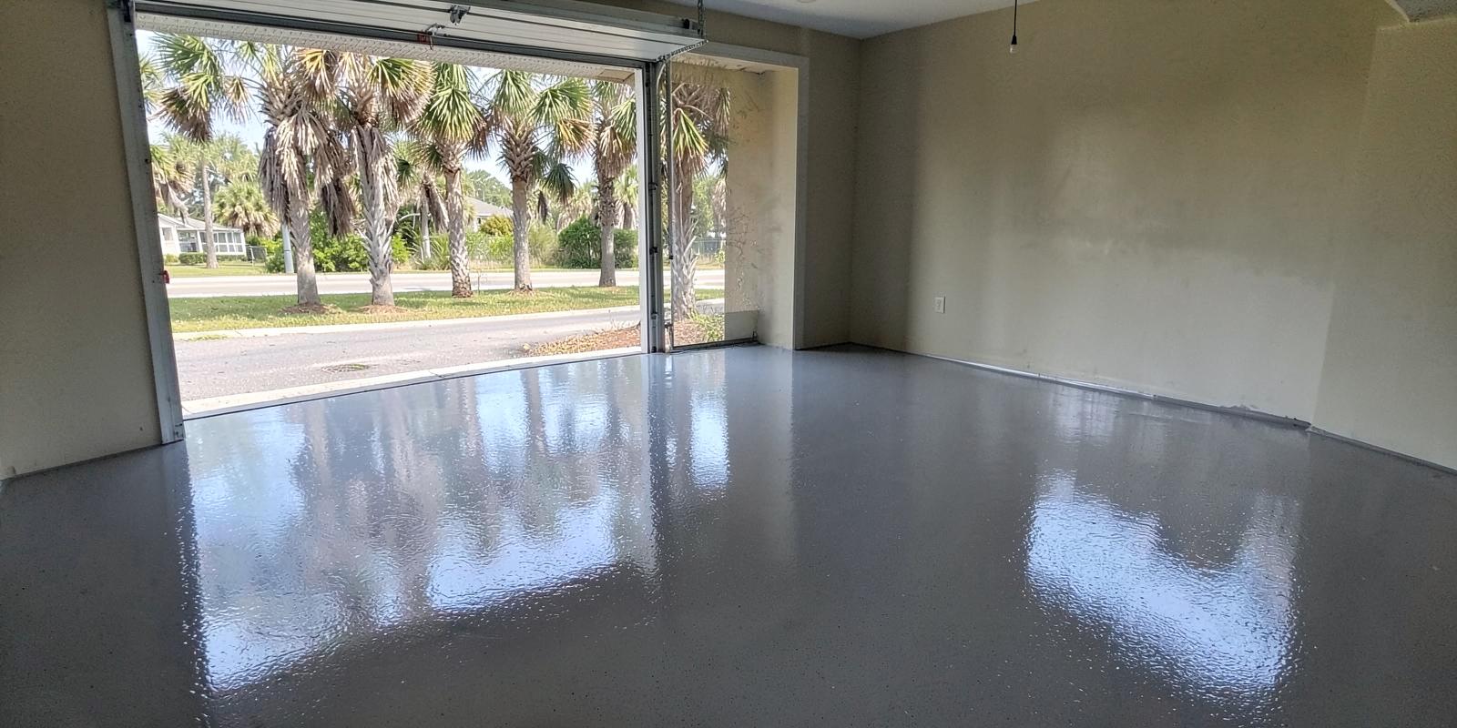 Freshly coated glossy gray epoxy garage floor with the door open onto a palmetto-lined coastal street