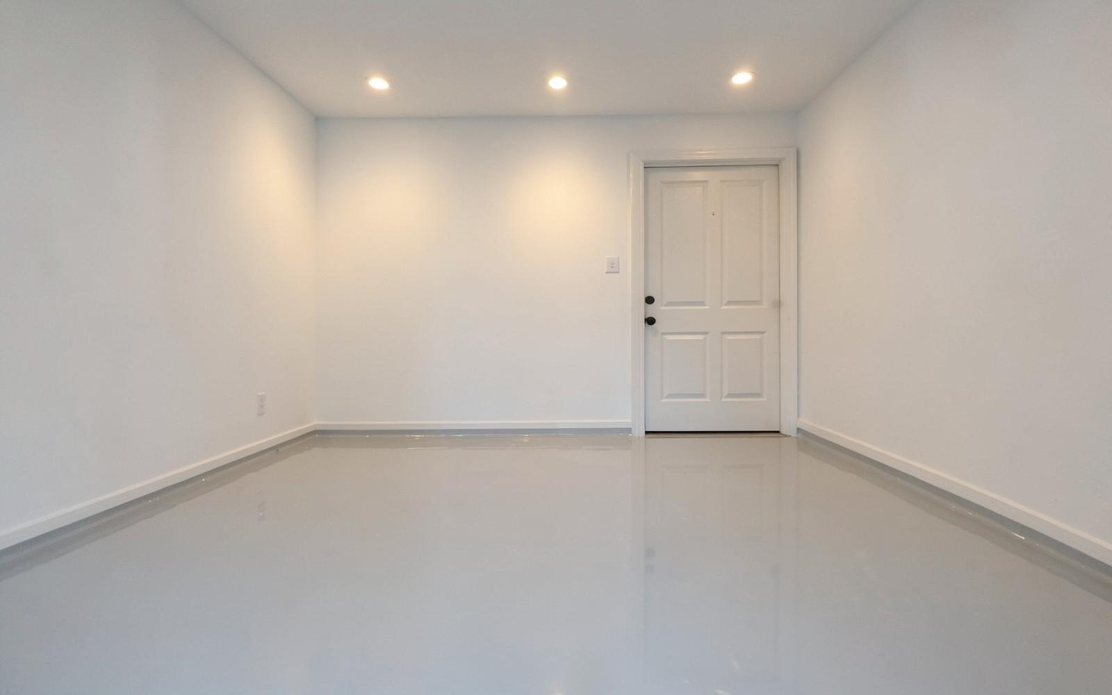 Glossy pale grey epoxy-coated floor in an empty spotless garage with plain white walls and warm recessed lighting