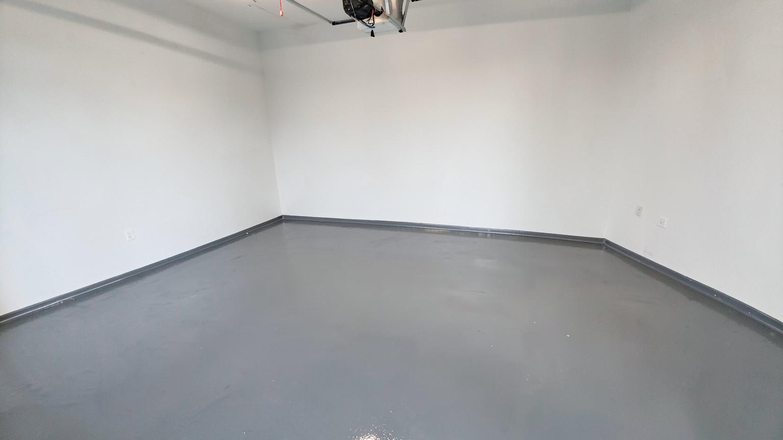 Glossy gray epoxy-coated garage floor in a clean empty garage with plain white walls