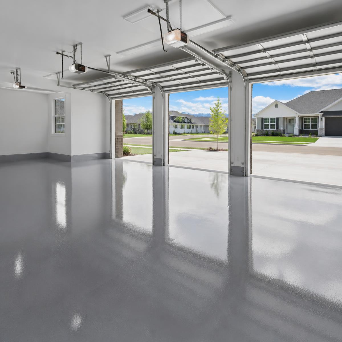 Glossy gray epoxy-coated floor in a clean empty three-car garage with the doors open to a sunny new neighborhood