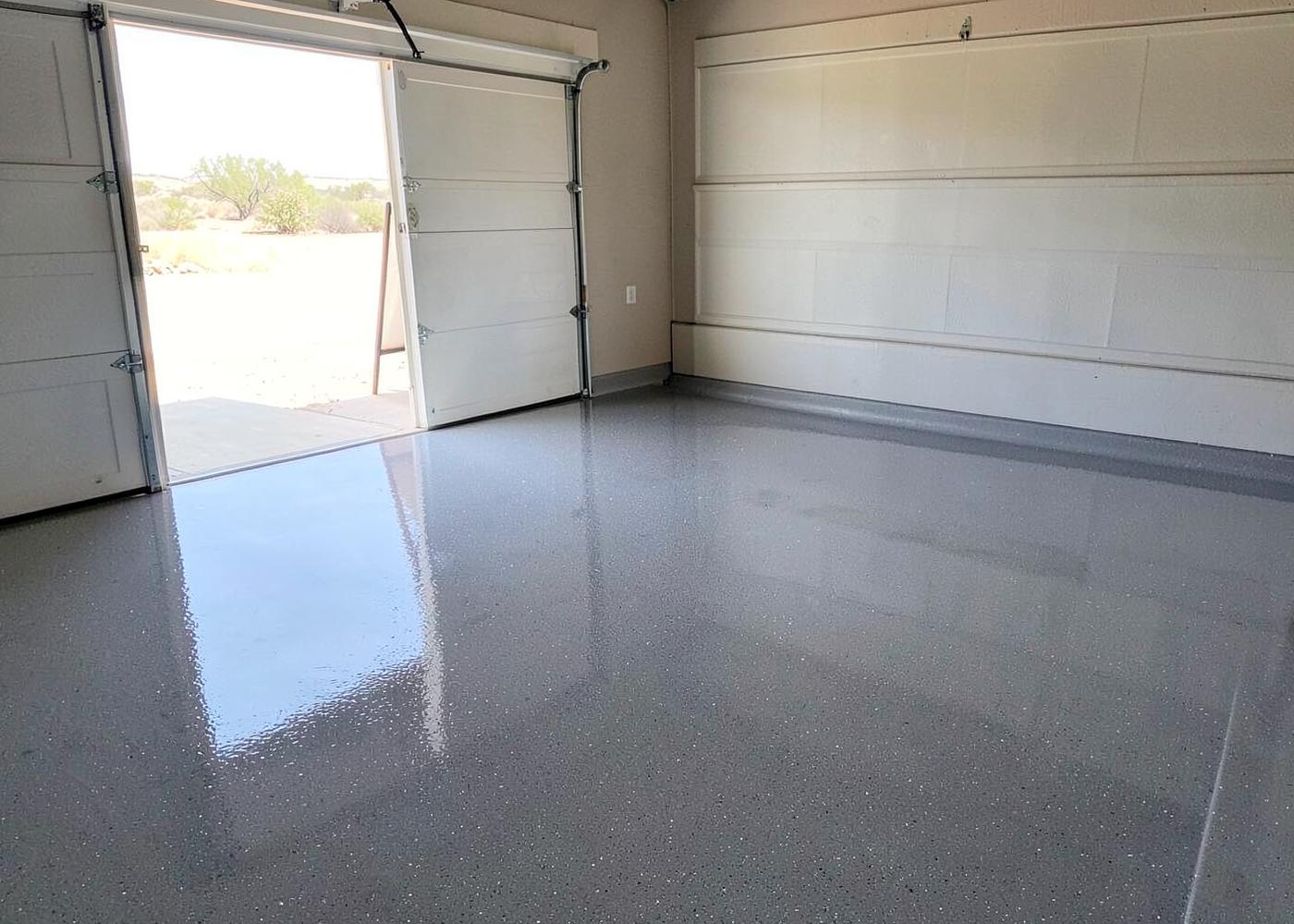 Freshly coated glossy grey flake epoxy garage floor in a clean residential garage with bright desert light through the open door