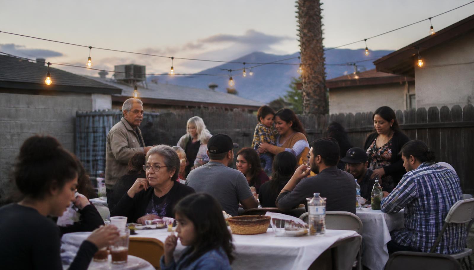 Multi-generational family gathered in a modest backyard at dusk with string lights strung overhead