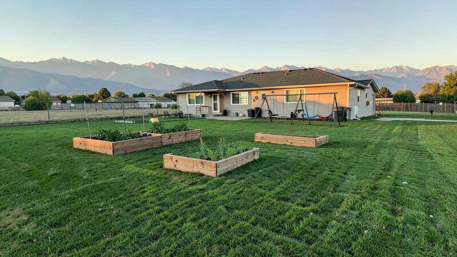 Large green backyard with raised garden beds and a swing set behind a single story home on a wide flat lot