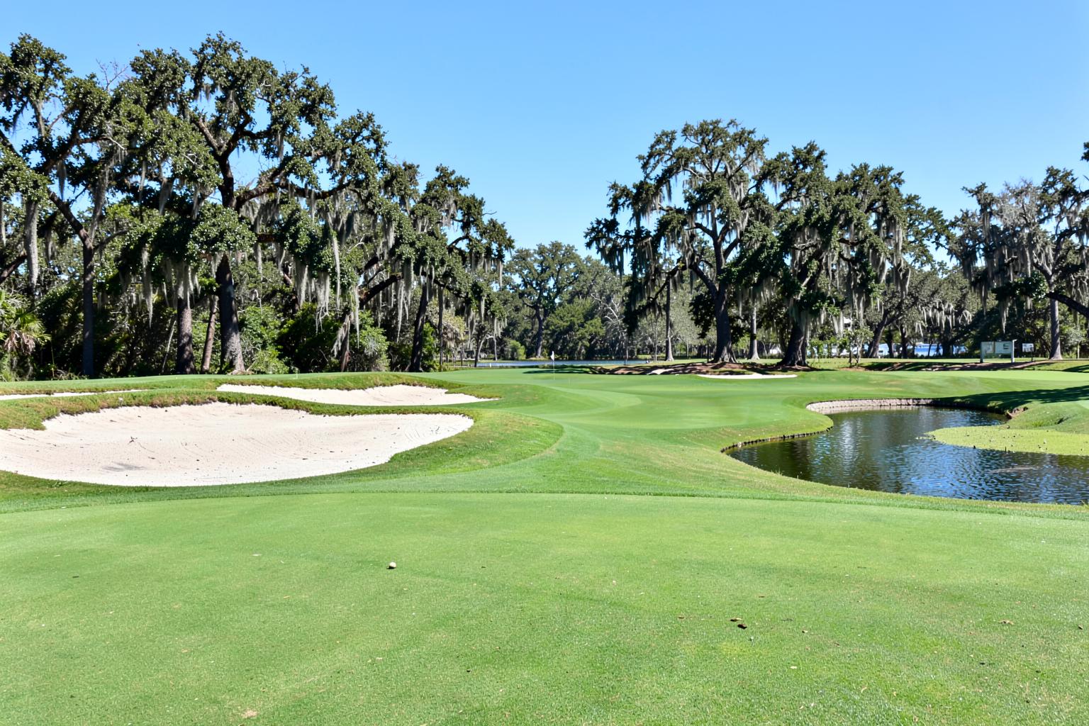 Sunny coastal golf fairway with sand bunkers, live oaks draped in moss and a pond