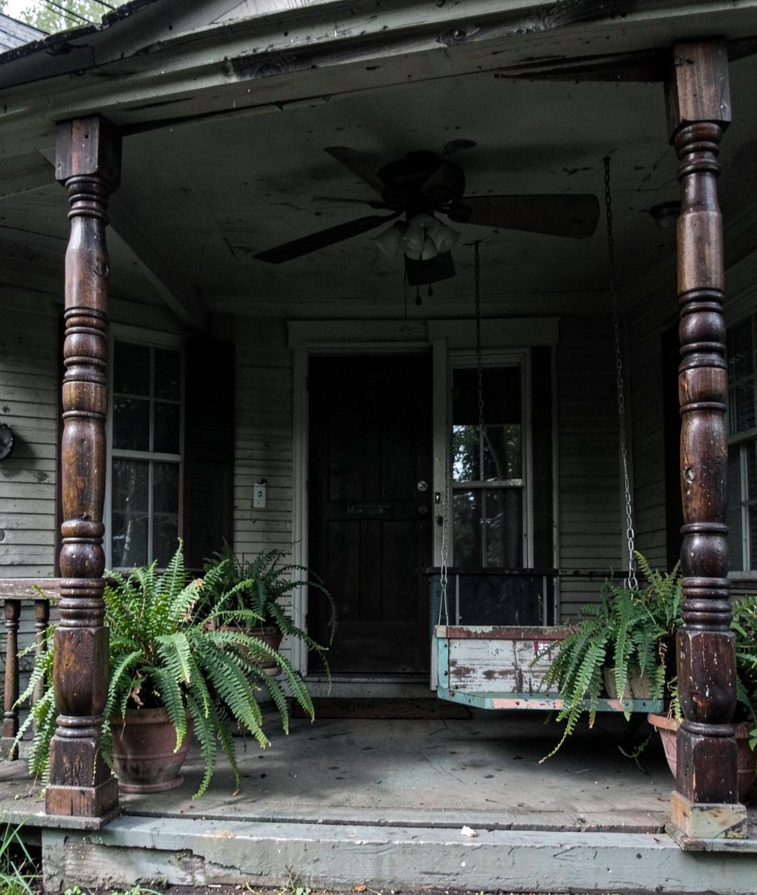 Deep shaded porch of an older Southern house with turned wooden columns, ceiling fan and hanging ferns