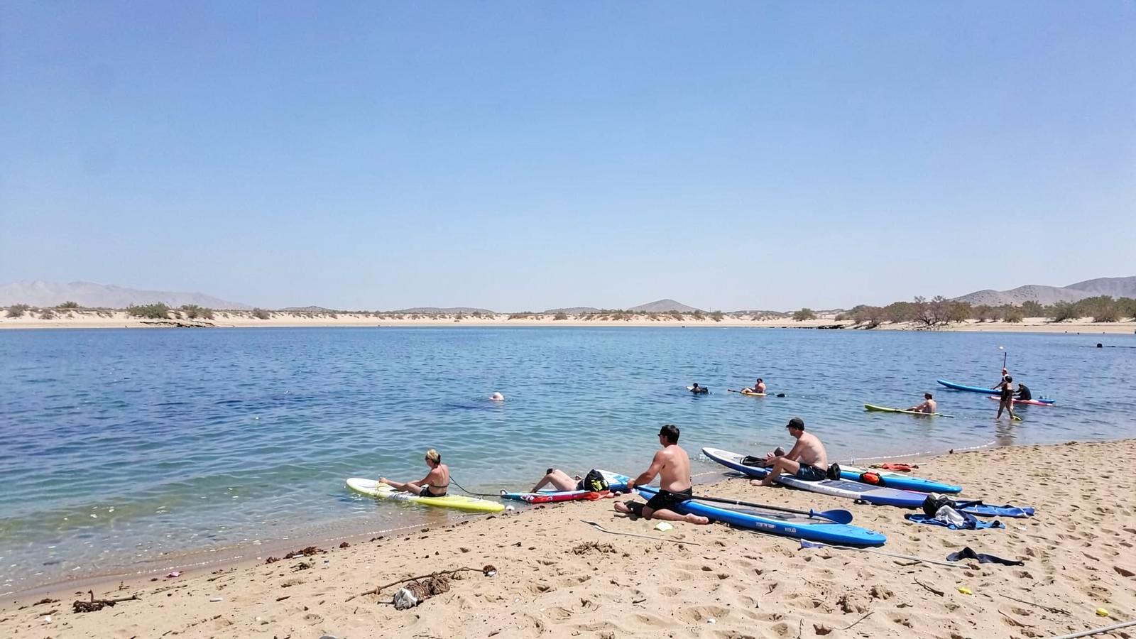 Sandy desert lake beach with clear blue water, scattered rocks and bare arid mountains across the bay
