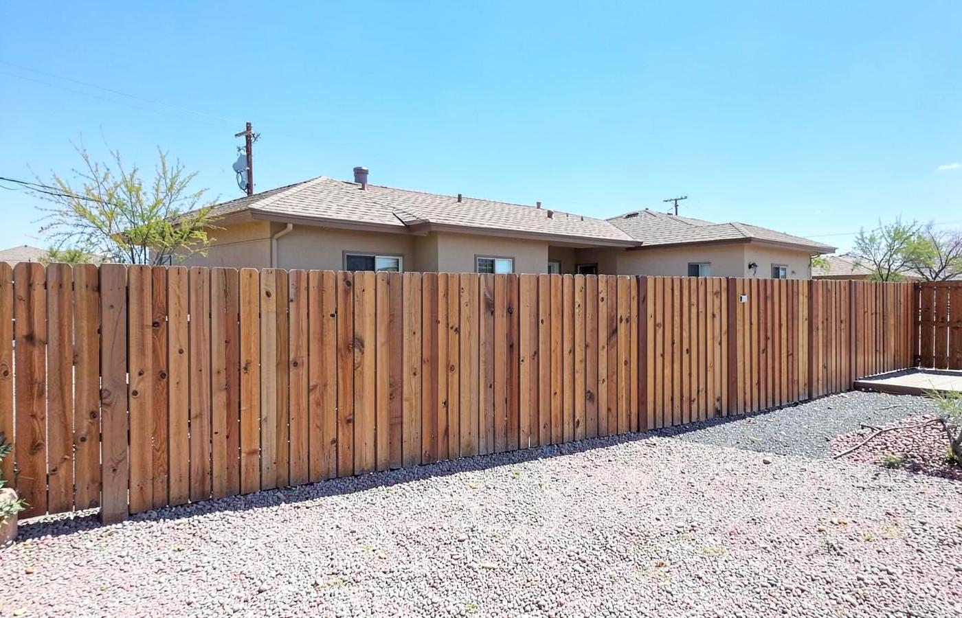 Newly installed wooden privacy fence along the gravel backyard of a modest desert home