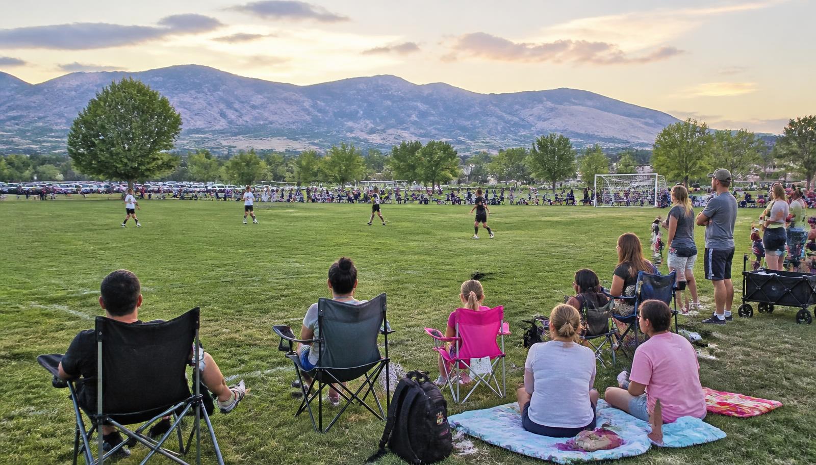 Neighborhood park soccer field with families gathered on the sidelines and mountains rising behind