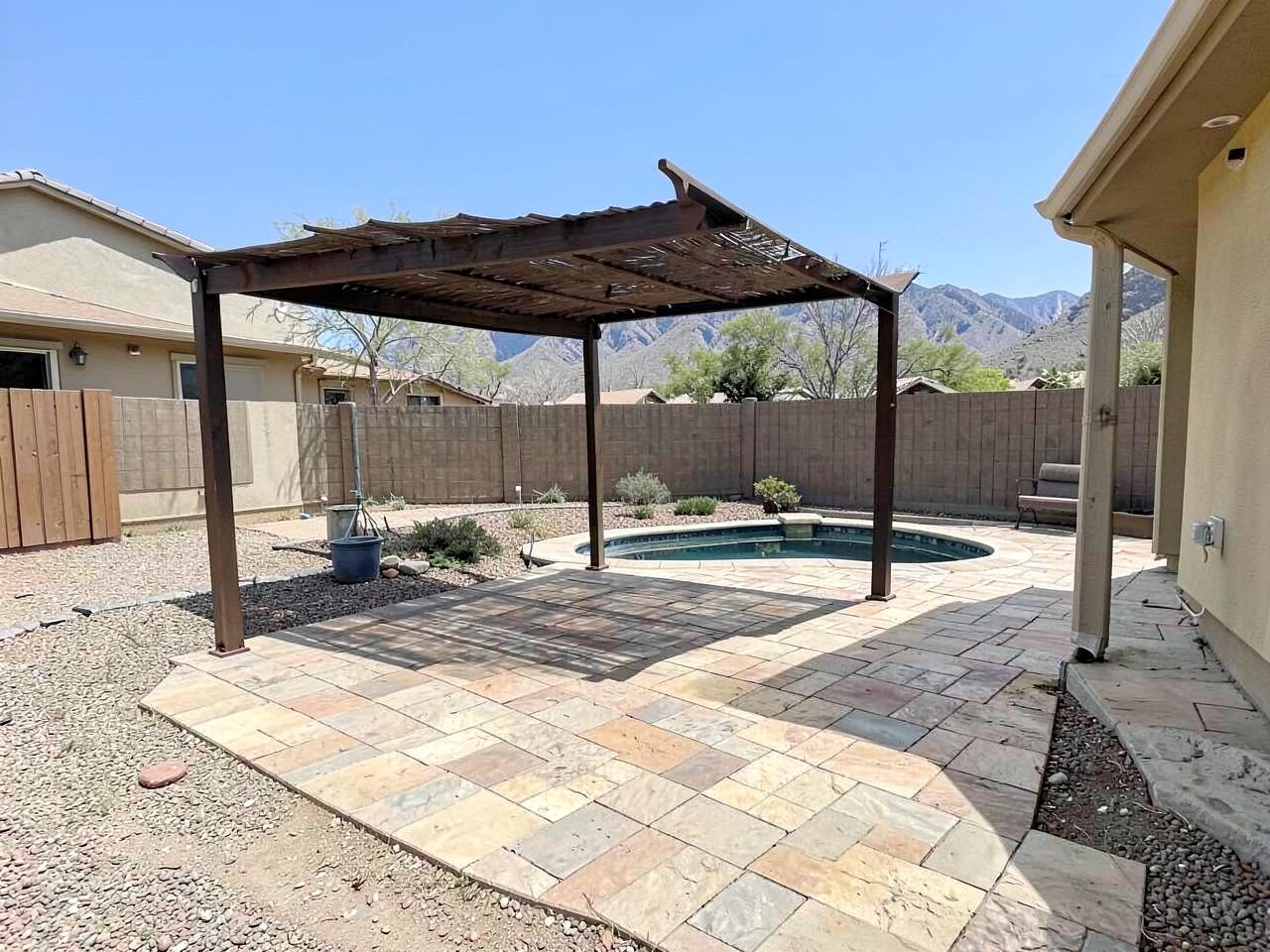 Desert backyard with a new travertine paver patio, pergola shade structure, and small pool below mountains