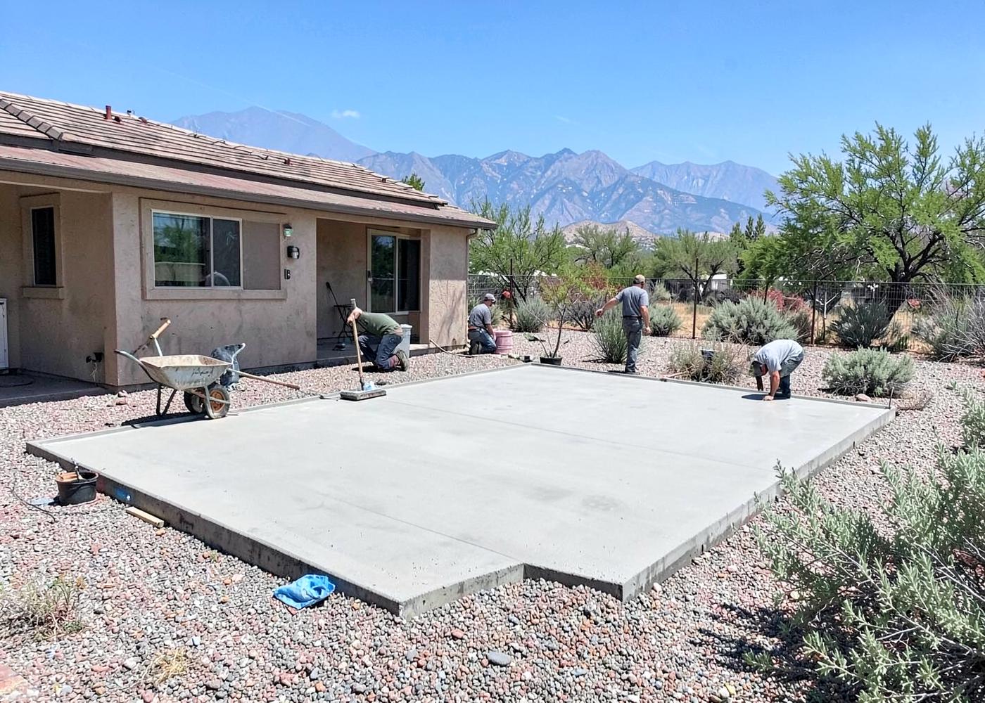 Concrete crew finishing a freshly poured backyard patio slab at a high-desert home with sagebrush and mountains beyond