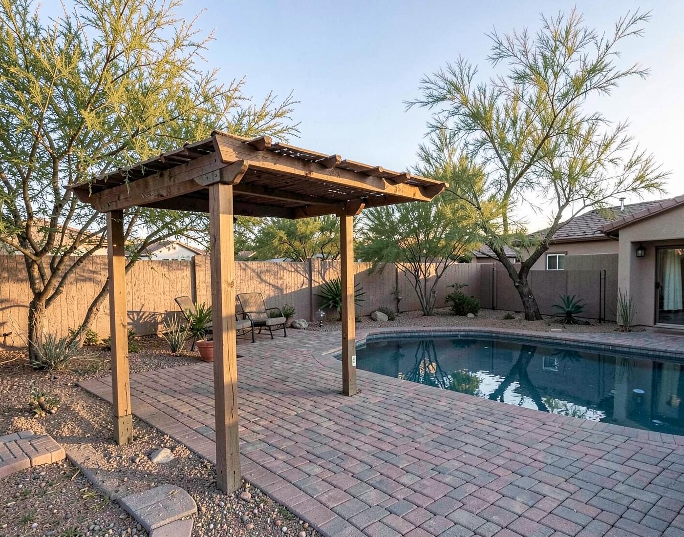 Backyard shade pergola over a paver patio beside a swimming pool at a desert home in late afternoon light