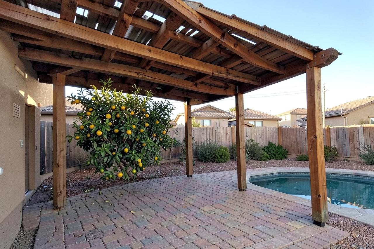 Wooden patio shade cover over paver decking beside a small pool and citrus tree at a desert suburban home
