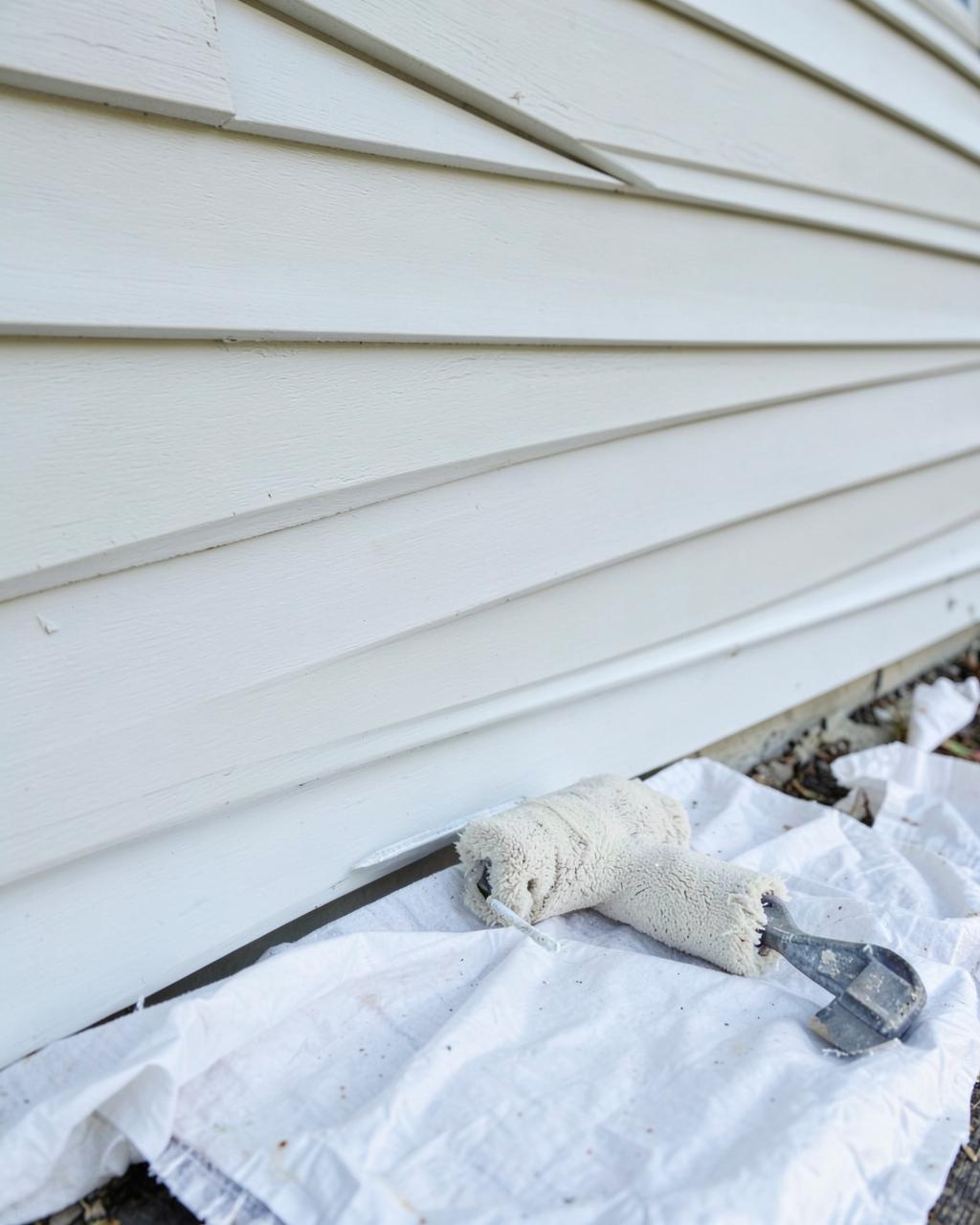 Freshly repainted white lap siding with a paint roller resting on a drop cloth below