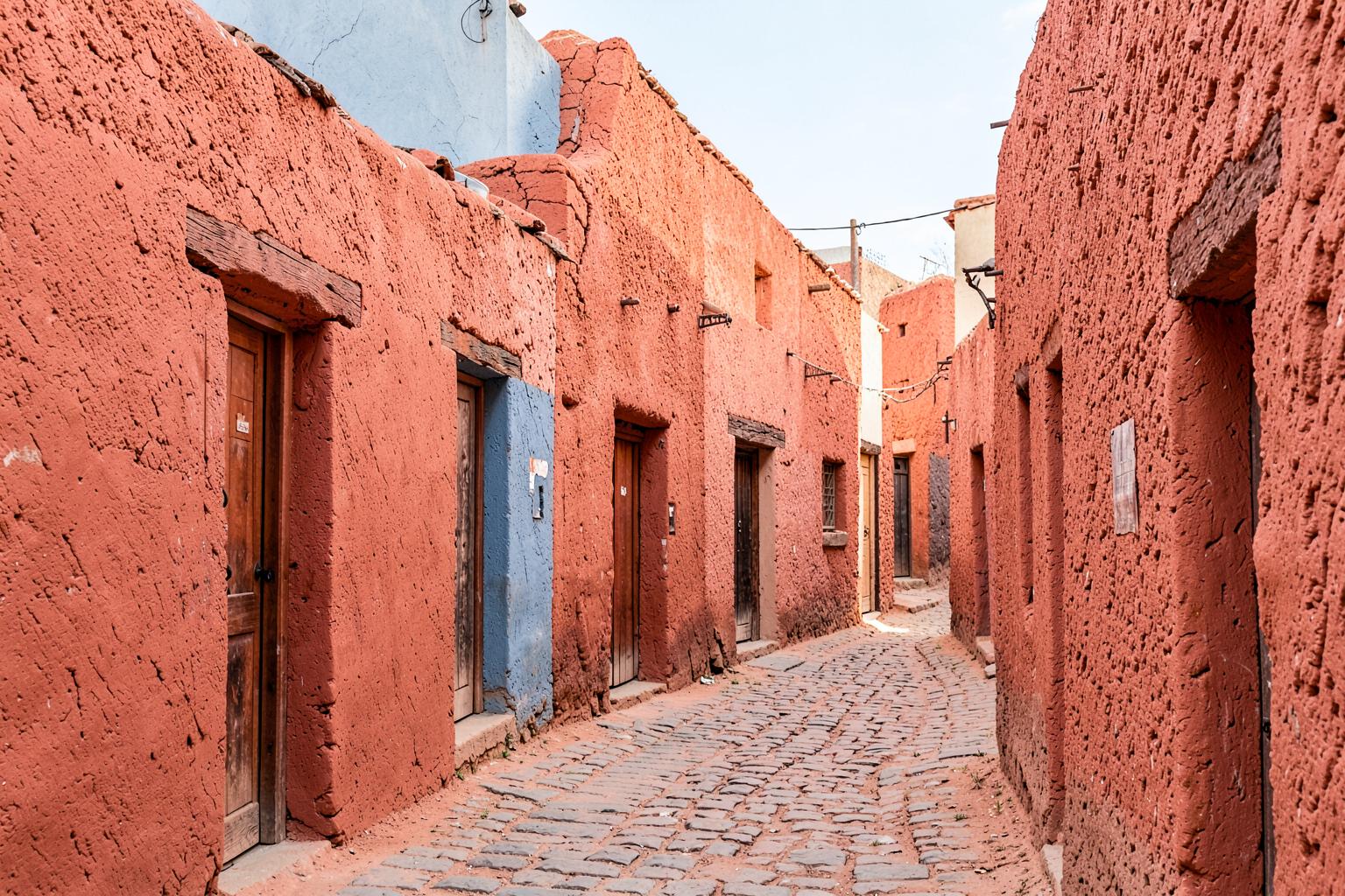 Narrow street of brightly painted thick adobe walls and wooden doors in a historic southwestern barrio